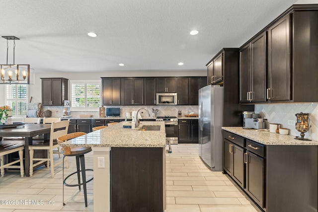 kitchen with pendant lighting, sink, light stone countertops, an island with sink, and appliances with stainless steel finishes