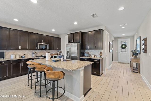 kitchen featuring a kitchen bar, a center island with sink, sink, light stone counters, and stainless steel appliances