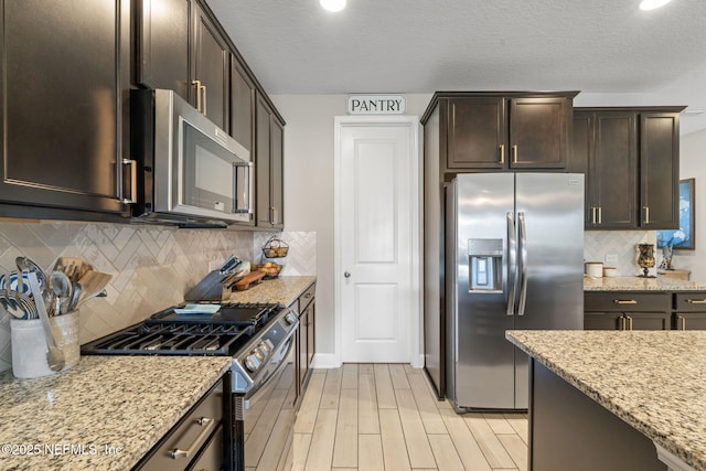 kitchen featuring light stone counters, dark brown cabinetry, appliances with stainless steel finishes, and tasteful backsplash