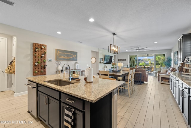 kitchen featuring light stone countertops, sink, hanging light fixtures, a center island with sink, and ceiling fan with notable chandelier