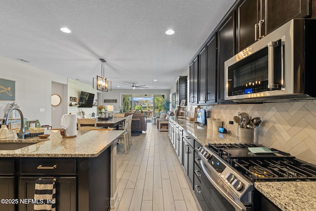 kitchen featuring backsplash, stainless steel appliances, ceiling fan, sink, and hanging light fixtures