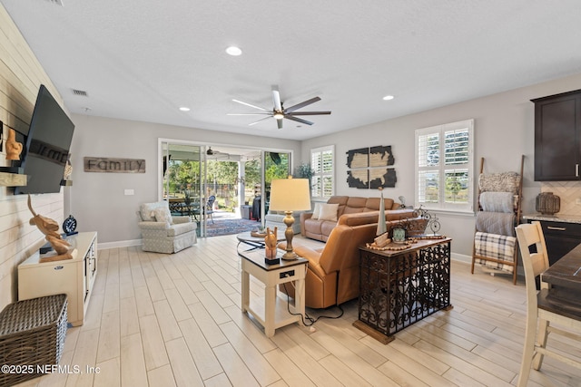 living room with light wood-type flooring, a textured ceiling, a wealth of natural light, and ceiling fan