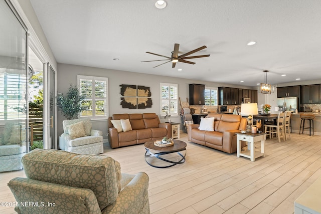 living room with plenty of natural light, ceiling fan with notable chandelier, and light hardwood / wood-style flooring