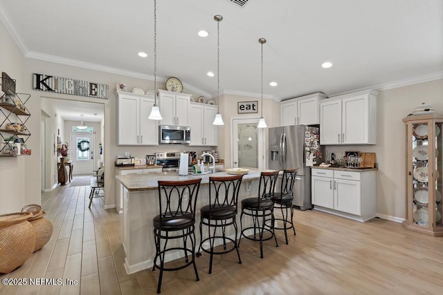 kitchen with light wood-type flooring, stainless steel appliances, white cabinets, hanging light fixtures, and an island with sink