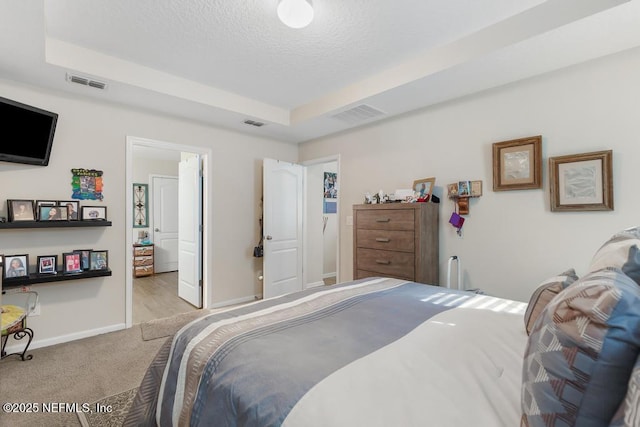 bedroom featuring light carpet, a textured ceiling, and a tray ceiling