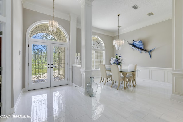 entrance foyer with decorative columns, french doors, a textured ceiling, and a notable chandelier