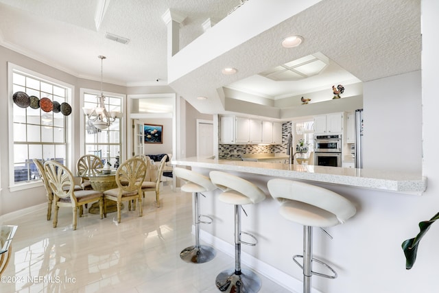 kitchen with double oven, kitchen peninsula, decorative backsplash, a breakfast bar, and white cabinets