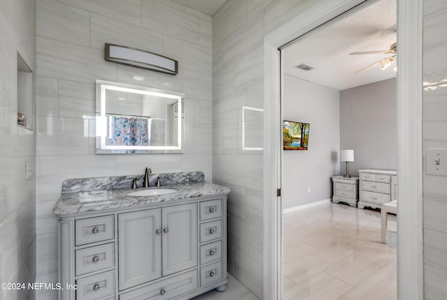 bathroom with vanity, a textured ceiling, ceiling fan, and tile walls