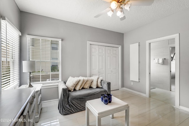 living room with a textured ceiling, ceiling fan, and light tile patterned flooring