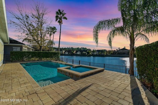 pool at dusk featuring an in ground hot tub, a water view, and a patio area