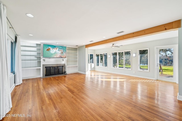 unfurnished living room featuring ceiling fan, light hardwood / wood-style floors, beam ceiling, and built in shelves