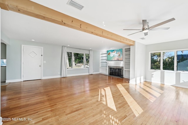 unfurnished living room featuring ceiling fan, wood-type flooring, built in features, and beamed ceiling