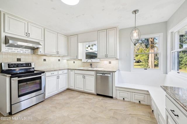 kitchen with white cabinetry, stainless steel appliances, decorative light fixtures, wall chimney range hood, and sink