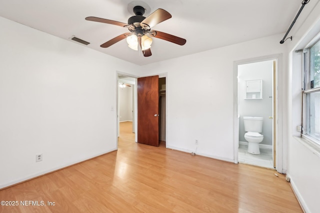 unfurnished bedroom with light wood-type flooring, ceiling fan, a closet, and ensuite bath