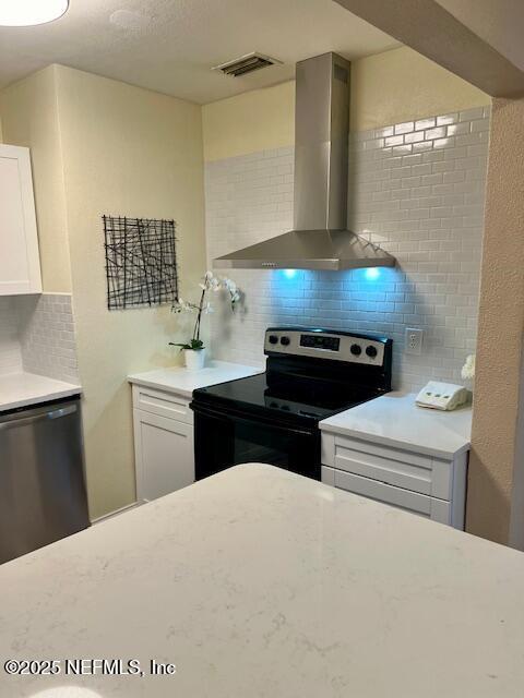 kitchen featuring decorative backsplash, white cabinetry, stainless steel appliances, and wall chimney range hood