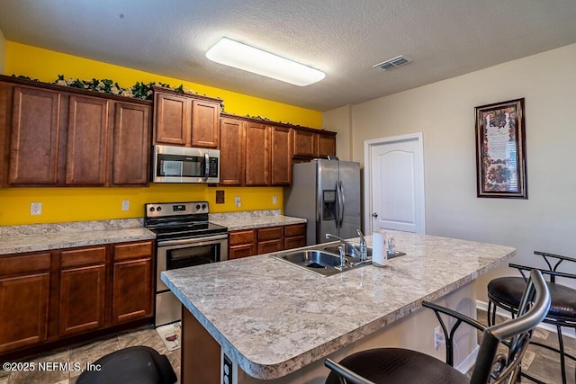 kitchen with sink, a textured ceiling, a breakfast bar area, a kitchen island with sink, and appliances with stainless steel finishes