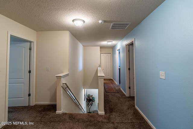 hall with a textured ceiling and dark carpet