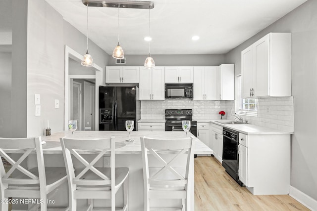 kitchen with sink, hanging light fixtures, a breakfast bar, white cabinets, and black appliances