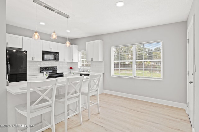 kitchen featuring decorative backsplash, a kitchen bar, black appliances, pendant lighting, and white cabinets