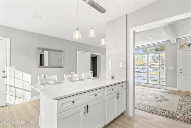 kitchen featuring light stone counters, light hardwood / wood-style flooring, beamed ceiling, pendant lighting, and white cabinets