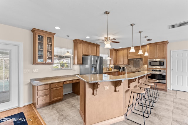 kitchen featuring light stone countertops, a healthy amount of sunlight, a kitchen bar, a kitchen island with sink, and appliances with stainless steel finishes