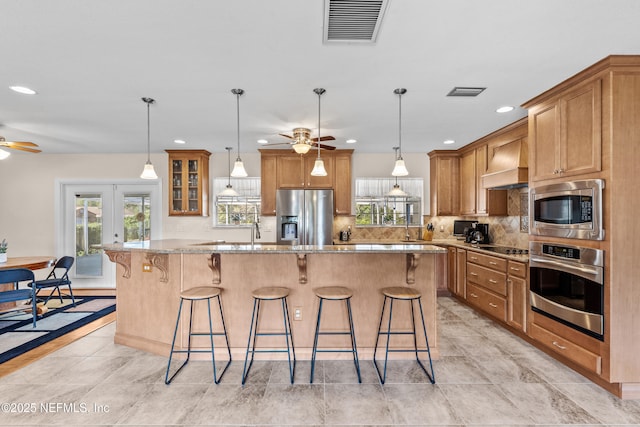 kitchen featuring light stone countertops, premium range hood, stainless steel appliances, a kitchen island, and a breakfast bar area