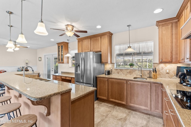 kitchen with a breakfast bar, a center island with sink, sink, stainless steel fridge, and decorative light fixtures