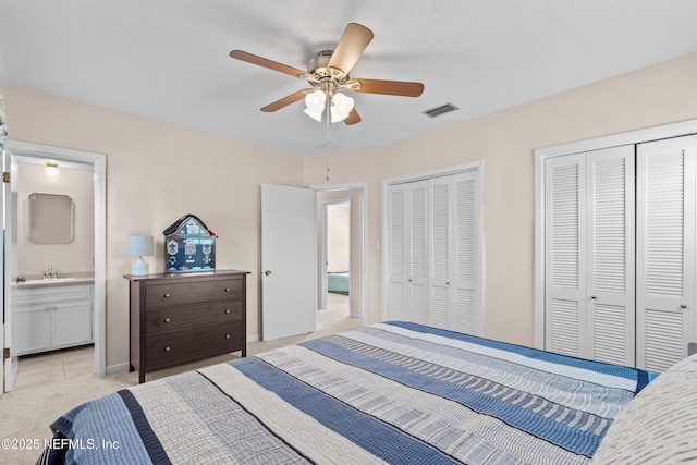 bedroom featuring two closets, sink, ceiling fan, connected bathroom, and light colored carpet