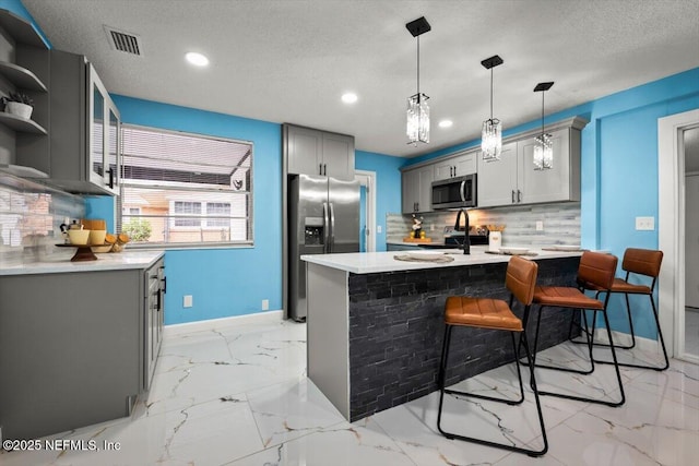 kitchen with a kitchen bar, gray cabinets, pendant lighting, stainless steel appliances, and backsplash