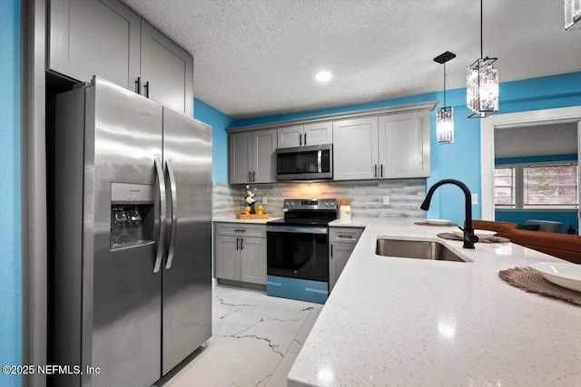 kitchen with gray cabinets, appliances with stainless steel finishes, tasteful backsplash, sink, and hanging light fixtures