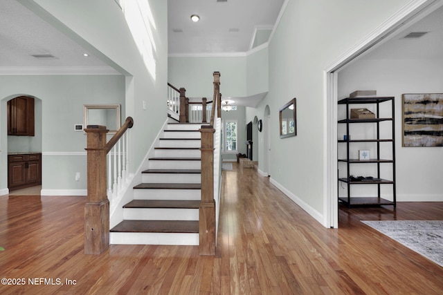 stairs featuring wood-type flooring, a high ceiling, and ornamental molding