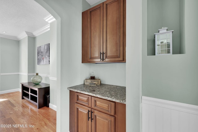 bar featuring light stone countertops, a textured ceiling, light hardwood / wood-style floors, and ornamental molding