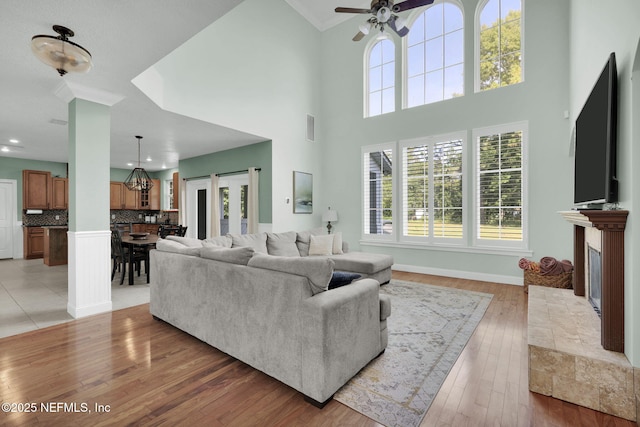 living room with ceiling fan, light hardwood / wood-style floors, a towering ceiling, and a fireplace