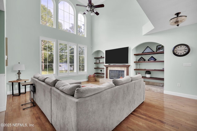 living room featuring hardwood / wood-style floors, ceiling fan, built in features, and a high ceiling