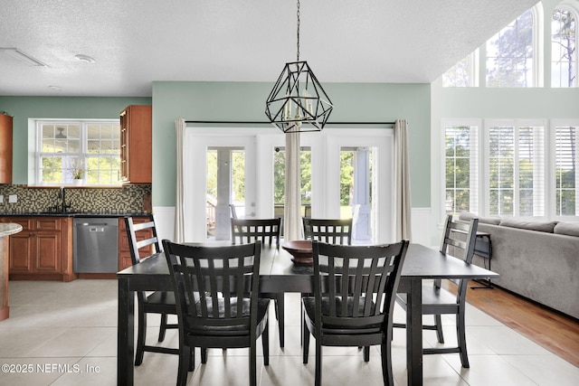 tiled dining room with sink, a healthy amount of sunlight, a textured ceiling, and a notable chandelier