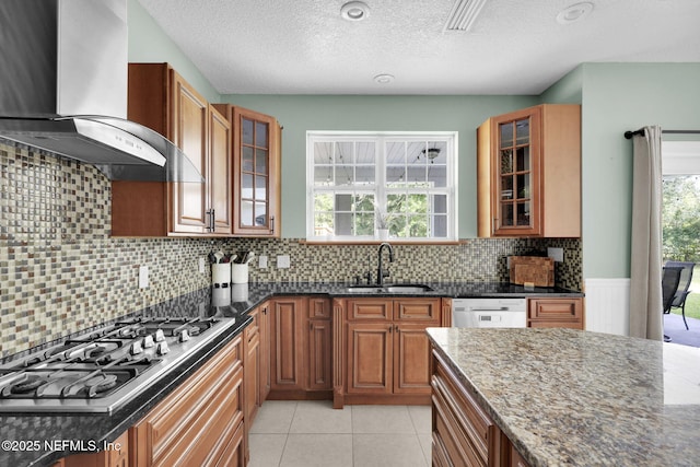 kitchen with sink, wall chimney exhaust hood, stainless steel gas cooktop, dark stone counters, and dishwashing machine