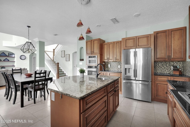 kitchen featuring tasteful backsplash, stainless steel appliances, sink, hanging light fixtures, and an island with sink