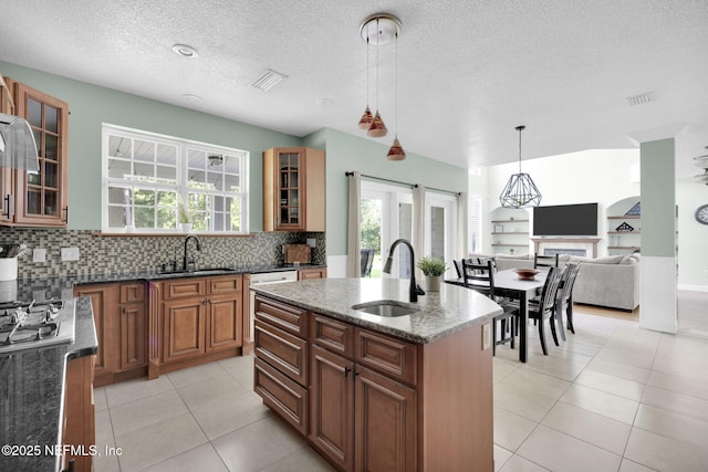 kitchen with dark stone countertops, sink, hanging light fixtures, and a center island with sink