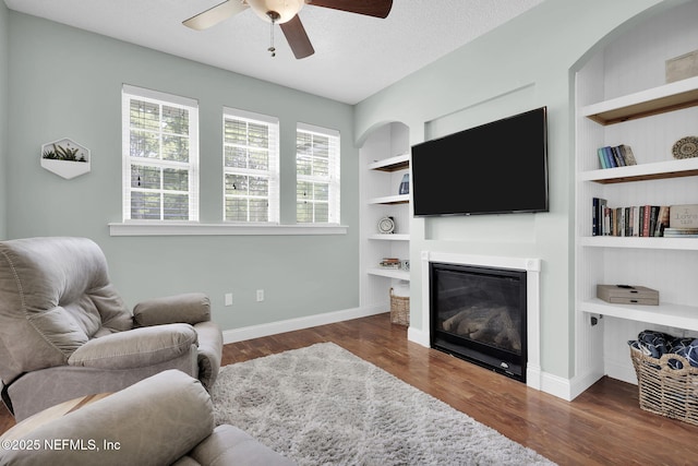 living room with a textured ceiling, dark hardwood / wood-style floors, built in features, and ceiling fan