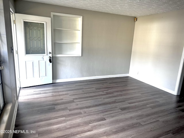 spare room with built in features, dark hardwood / wood-style floors, and a textured ceiling