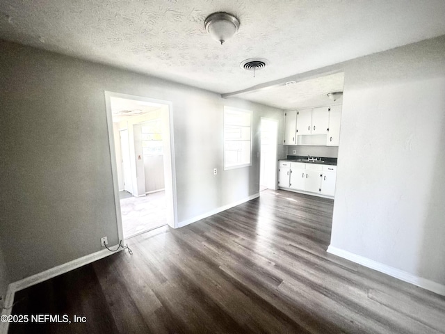 unfurnished living room featuring dark hardwood / wood-style floors, sink, and a textured ceiling