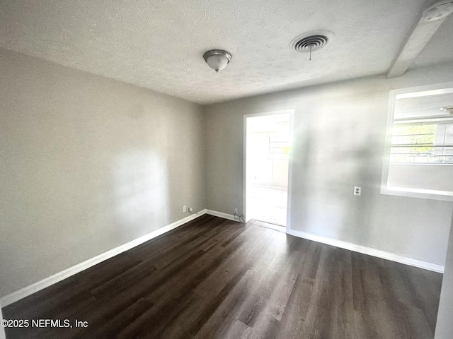 spare room featuring beamed ceiling, dark wood-type flooring, and a textured ceiling