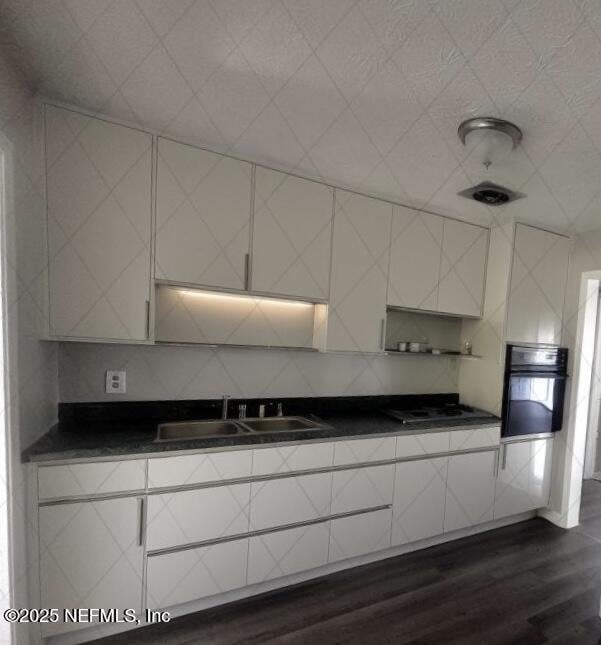 kitchen featuring sink, dark wood-type flooring, black oven, gas cooktop, and tasteful backsplash