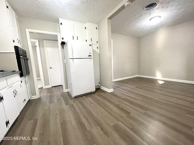 kitchen with black oven, wood-type flooring, white cabinets, white fridge, and a textured ceiling