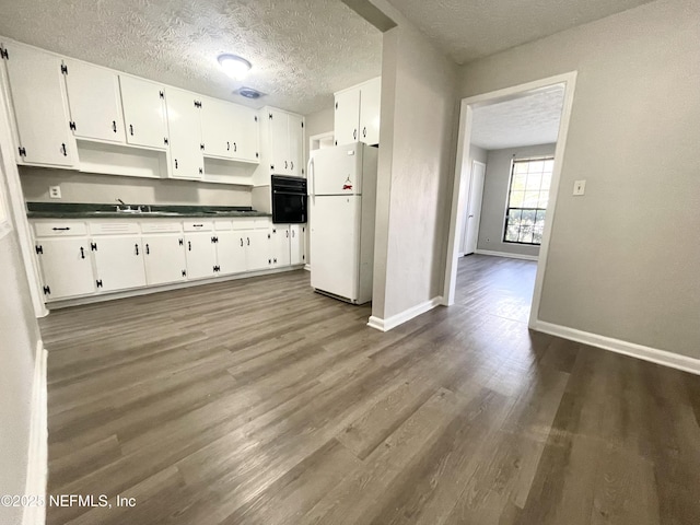 kitchen with a textured ceiling, white refrigerator, dark hardwood / wood-style floors, oven, and white cabinets