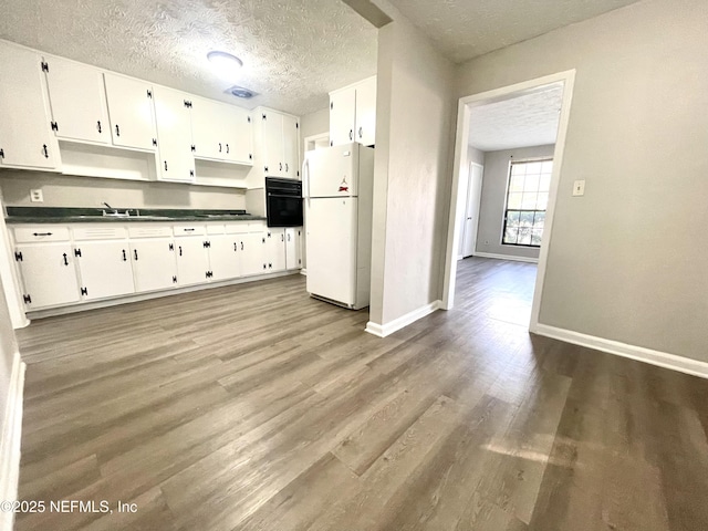 kitchen with hardwood / wood-style floors, black oven, white cabinets, white refrigerator, and a textured ceiling