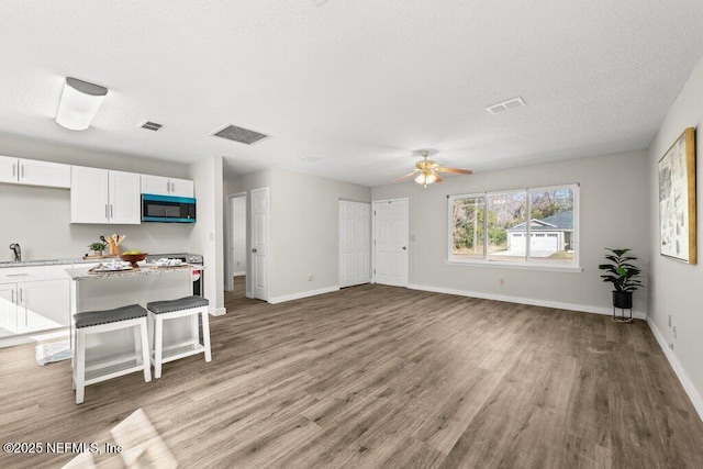 kitchen with a breakfast bar, wood-type flooring, sink, white cabinets, and ceiling fan