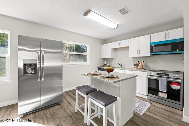 kitchen with a kitchen bar, appliances with stainless steel finishes, white cabinetry, and dark hardwood / wood-style floors