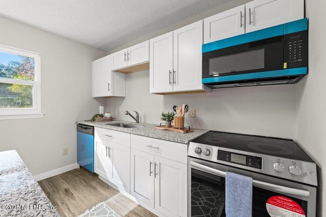 kitchen featuring appliances with stainless steel finishes, light wood-type flooring, a textured ceiling, sink, and white cabinetry