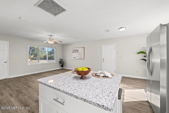 kitchen with hardwood / wood-style floors, light stone countertops, a center island, stainless steel fridge, and white cabinetry